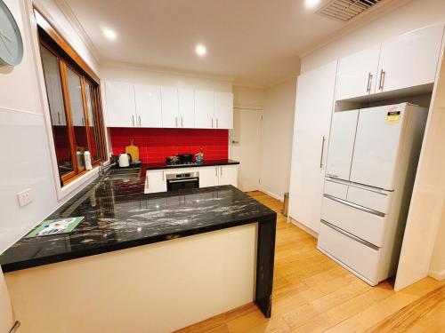 une cuisine avec des armoires blanches et un comptoir noir dans l'établissement Modern 2 bedroom home in burwood east, à Burwood East