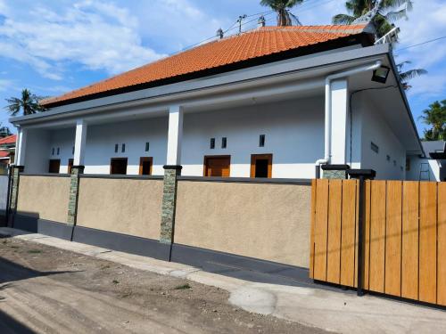 a white house with an orange roof and a fence at Gama Stay in Lovina