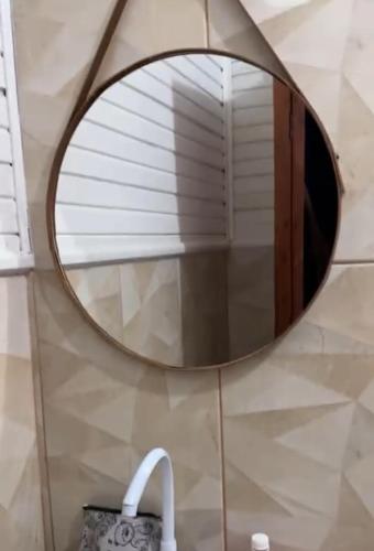 a round mirror hanging on a wall in a bathroom at Aconchegante demais in Macapá