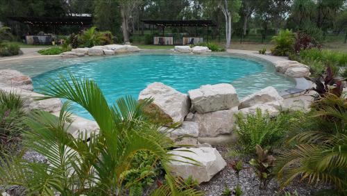 a swimming pool with rocks in a garden at Litchfield Safari Camp in Rakula