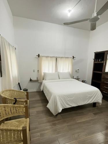 a bedroom with a white bed and two chairs at Casa "Cerca del Mar" in Mazunte