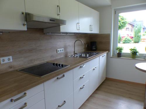 cocina con armarios blancos, fregadero y ventana en Ferienwohnung Lerchenweg en Möhnesee