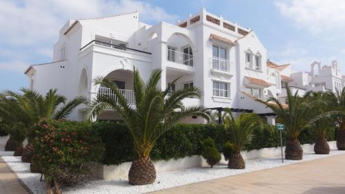 a white building with palm trees in front of it at Apartamentos Golf Center in Roquetas de Mar