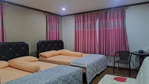 a room with two beds and a table and pink curtains at Ban Roi Pah in Ban Khlong Si