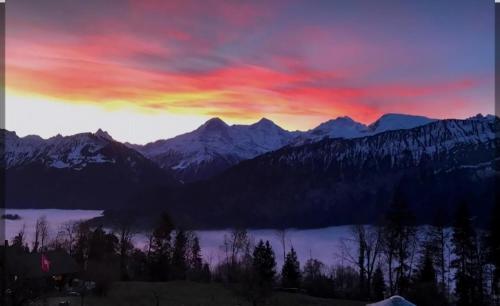 a sunset over a snowy mountain range with a lake at Einzigartige Holzhütte Mit Bergpanorama in Beatenberg