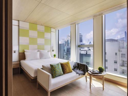 a bedroom with a bed and a couch in front of a window at AKI Hotel Hong Kong - MGallery Collection in Hong Kong