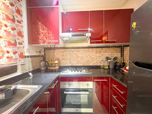 La cuisine est équipée de placards rouges et d'un four avec plaques de cuisson. dans l'établissement Palmeraie chic à 10 mn du stade Piscine et confort, à Dar Caïd Layadi