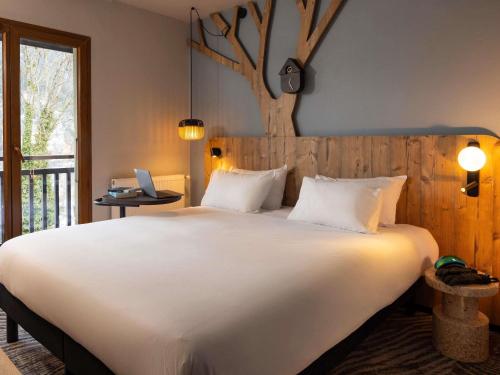 a bedroom with a large white bed with a tree on the wall at ibis Styles Les Houches Chamonix in Les Houches