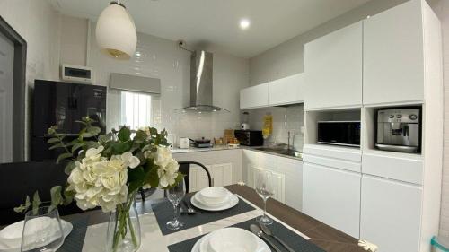 Двухкомнатный дом на Бангтао ДИН في Ban Thalat Choeng Thale: مطبخ أبيض مع إناء من الزهور على طاولة