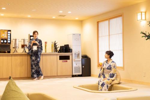 a woman standing in a room with another woman sitting in a room at Ooedo Onsen Monogatari Premium Yoshinoya Irokuen in Kaga