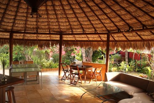 a patio with a table and chairs under a straw roof at Pousada Villa Botânica in Aracati