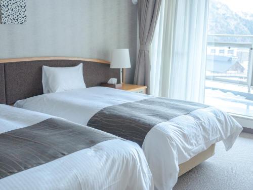 two beds in a hotel room with a window at GLOBAL RESORT NUKUI in Akiota