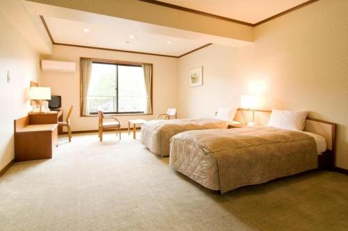 Una habitación de hotel con dos camas, un escritorio y una ventana. en HOTEL WINDSOR, en Nakatsugawa