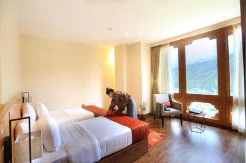 Una habitación de hotel con una cama y una persona de pie sobre ella. en The Pema by Realm, en Thimphu