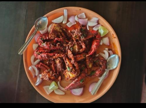 a plate of food with meat and onions and spoons at Adhvaya stay in in Kumta