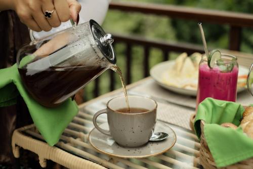 una persona che versa il caffè in una tazza su un tavolo di Orchid Ubud Cottage ad Ubud