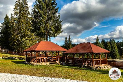 twee prieeltjes met rode daken in een park bij Bucsin menedékház in Bucin