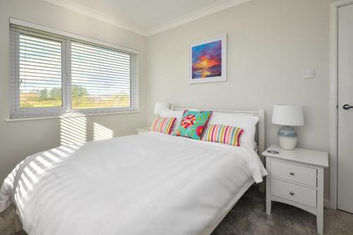 a white bedroom with a white bed and a window at Maes Coch in Abersoch