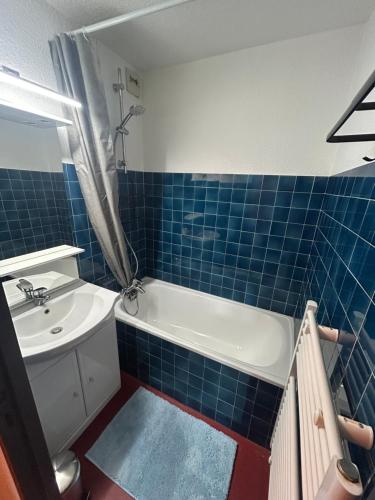 ein blau gefliestes Bad mit einer Badewanne und einem Waschbecken in der Unterkunft Appartement cosy quartier Napoléon in Val Cenis