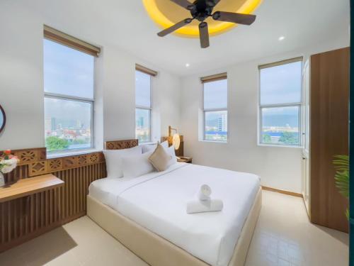 a bedroom with a large white bed with windows at Sujet Beach Hotel and Apartment Danang by Haviland in Da Nang