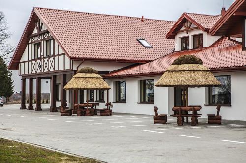 ein Gebäude mit Tischen und Strohschirmen auf einem Parkplatz in der Unterkunft Maciejowa Chata Stare Lubiejewo in Ostrów Mazowiecka