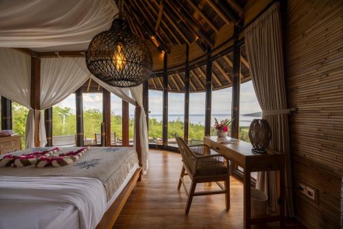 a bedroom with a bed and a desk and windows at Ketanu Bamboo Lodge Sumba in Praikalogu