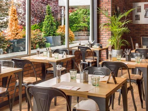 een restaurant met houten tafels, stoelen en ramen bij Novotel Paris Est in Bagnolet