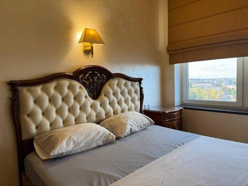 a bedroom with a bed with a large headboard and a window at Дельмар Люкс in Dnipro