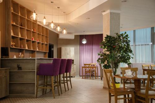 a restaurant with a bar with purple chairs and tables at Baitau Hotel Aktobe in Aktobe