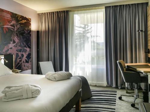 a hotel room with a bed and a desk and a window at Novotel Narbonne Sud A9/A61 in Narbonne