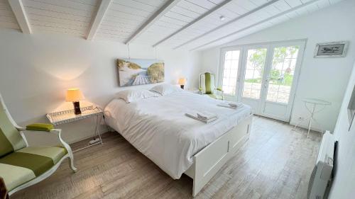 ein weißes Schlafzimmer mit einem großen Bett und einem Stuhl in der Unterkunft Dans le centre du village d'ARS EN RE, charmante villa bien décorée in Ars-en-Ré