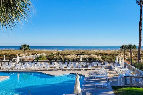 a pool with white chairs and umbrellas and the beach at Ocean One 215 in Hilton Head Island