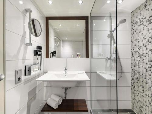 a white bathroom with a sink and a shower at Mercure Hotel Duisburg City in Duisburg