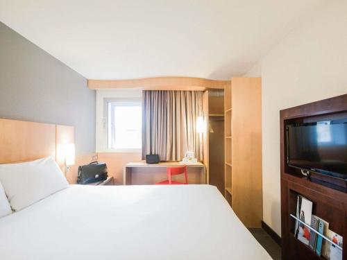 a hotel room with a bed and a flat screen tv at ibis London Heathrow Airport in Hillingdon