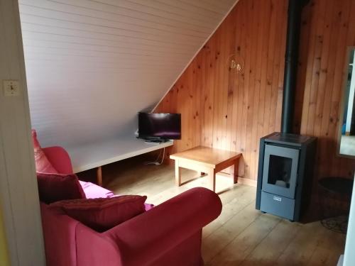 ein Wohnzimmer mit einem roten Sofa und einem Herd in der Unterkunft Les chalets au bord de l'étang de Malleteix in Champagnat