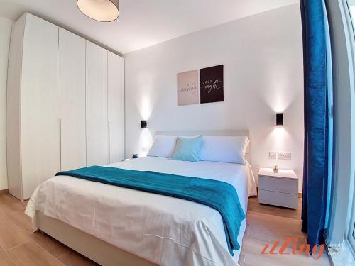 a white bedroom with a large bed with blue sheets at Balcony Apartment in Charming Malta Village in Hal Ghaxiak