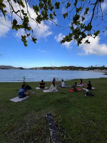 a group of people sitting on the grass by the water at Nômades Vibe da Ilha - Adventure Hostels in Florianópolis