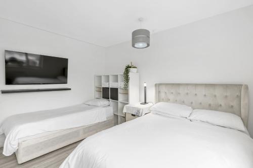 a white bedroom with two beds and a tv at Pass the Keys Modern 3Bed Garden Parking Nr Hainault Station in Chigwell