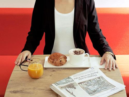 una persona sentada en una mesa con un plato de pan y una taza de café en ibis Sisteron, en Sisteron