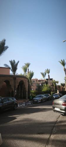 Una calle con coches aparcados en un aparcamiento con palmeras. en Riad Naim, en Marrakech