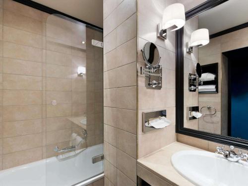 a bathroom with a sink and a tub and a mirror at Hotel Rotary Geneva - MGallery in Geneva