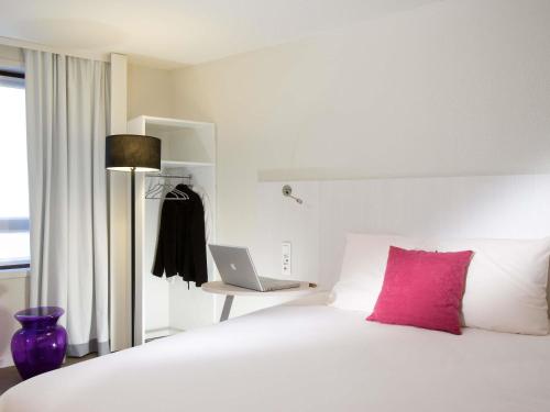 a white bed with a pink pillow and a laptop at ibis Styles Lille Centre Gare Beffroi in Lille