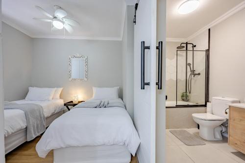 a white bedroom with two beds and a shower at Atlantic Haven in Bloubergstrand