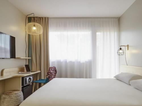 a hotel room with a white bed and a window at ibis Thalassa Hyeres Plage in Hyères