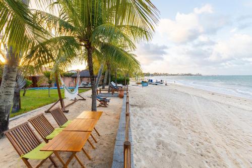 einen Strand mit Bänken und Palmen und dem Meer in der Unterkunft Casa Mar: vista e acesso à praia | By Carpediem in Jacumã
