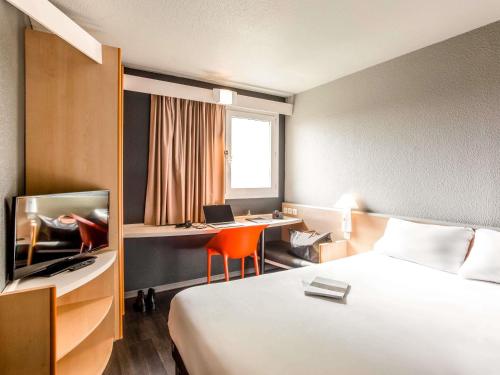 a hotel room with a bed and a desk and a tv at ibis Pau Lescar in Lescar