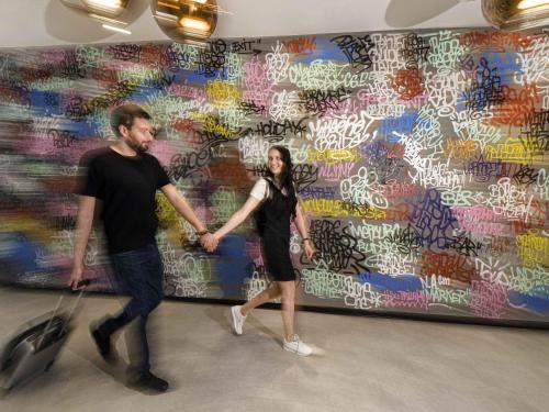 a man and woman holding hands in front of a wall with graffiti at Mercure Budapest Castle Hill in Budapest