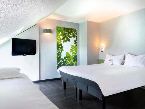 a bedroom with two beds and a tv on the wall at ibis Strasbourg Sud La Vigie in Ostwald