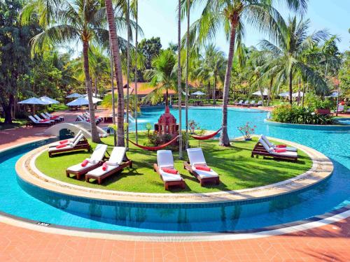 a pool at a resort with lounge chairs and palm trees at Sofitel Angkor Phokeethra Golf & Spa Resort in Siem Reap