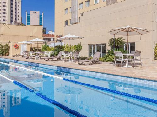 einen Pool mit Stühlen, Tischen und Sonnenschirmen in der Unterkunft Mercure Sao Paulo Vila Olimpia in São Paulo